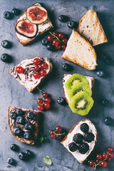Variety of dessert sandwiches with berries and cream cheese and chocolate swirl. Red currant, blueberries, sliced kiwi, figs over gray metal background. Flat lay, summer appetizer concept