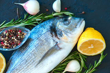 Close up of fresh raw dorado fish, rosemary herb garlic pepper and half of lemon on a black slate background. Overhead view.