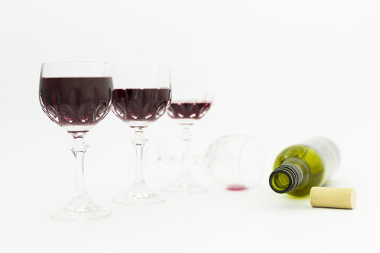 Concept of alcohol consumption, alcoholism and abuse with a line of beautiful crystal glasses filled with red wine and an empty bottle. Stages of drinking underlined by blurred image effect.