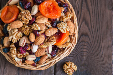 Fototapeta na wymiar Mix of nuts and dry fruits in a wooden plate. Assortment of walnuts, almonds, roasted cashews, pistachios, dry apricots, cranberries and raisins. Copy space and selective focus.