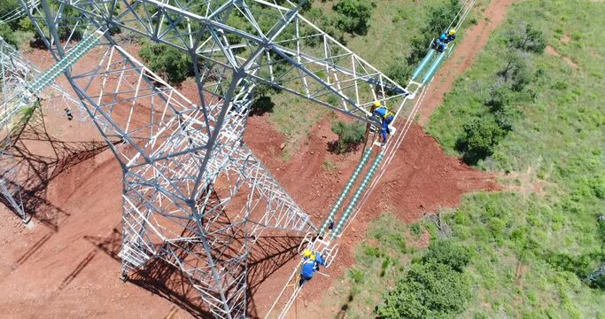 aerial drone of men working on a high steel electrical cable pylon tower with background of mountains farmland clouds and blue sky