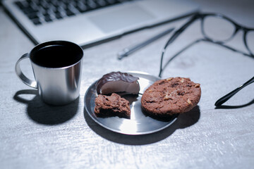 office working desk with laptop, pen and and glasses and coffee with cookie and sweets