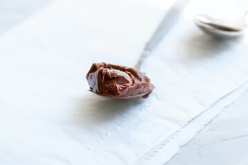 Melted chocolate paste in a spoon on a white stone background. Close up and copy space.