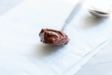 Fototapeta premium Melted chocolate paste in a spoon on a white stone background. Close up and copy space.
