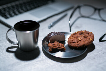 office working desk with laptop, pen and and glasses and coffee with cookie and sweets