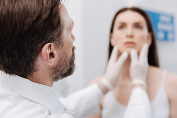 Fototapeta premium Gentle focused plastic surgeon examining patients face