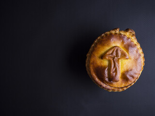 Small decorative mushroom pie with golden crust isolated on black background
