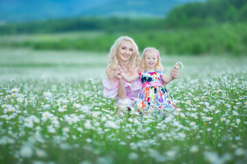 Blond mother with cute little daughter wearing white colourful pink dresses in chamomile field, summer time Enjoying spending time together happy childhood