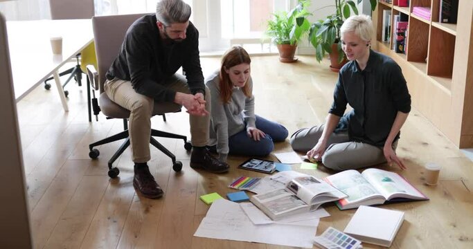 Overhead shot group of designers discussing ideas with paperwork on office floor