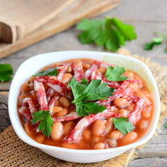 Red bean stew with smoked sausage, tomato sauce and fresh parsley in a bowl and on a wooden vintage table. Easy slow cooker red bean. Homemade red bean recipe. Closeup
