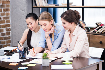 Multiethnic group of young businesswomen working together at table with papers
