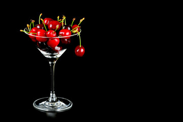Kirschen im Cocktailglas vor schwarzem Hintergrund mit Textfreifeld