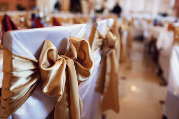 Ribbons of golden cloth pinned to white chairs which stand at dinner tables