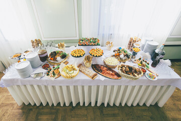 Large dishes with salty snacks stand on white dinner table