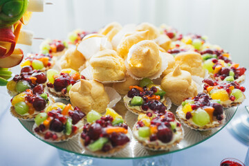 Baked baskets with berries and eclairs with white cream served on mirror dish