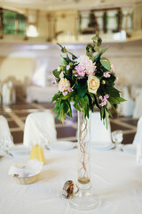 Bouquet of greenery stands in tall glass vase in the middle of dinner table