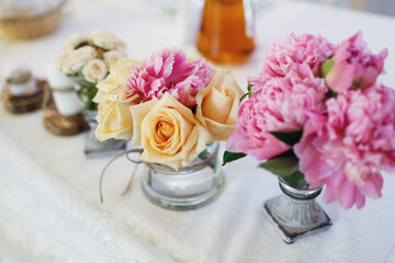 Tiny bouquets of roses and peonies stand on white table