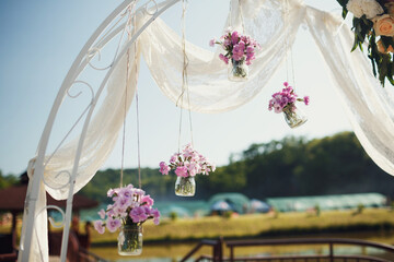 Glass bottles with pink flowers hang from wedding altar