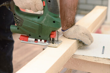 The master saws a wooden beam with a jigsaw