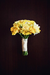 Yellow rose boutonniere, bouquet and wedding rings lie on dark wooden table
