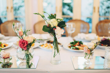 Little bouquets of roses stand on white dinner table