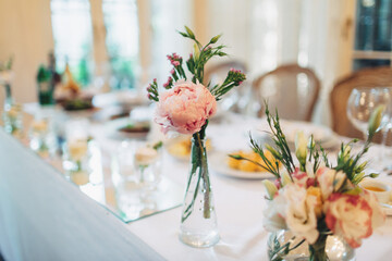Little bouquets of peonies stand on white dinner table