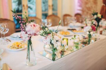 Little bouquets of peonies stand on white dinner table