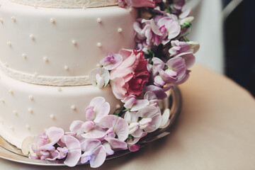 White wedding cake decorated with violet garland of orchids