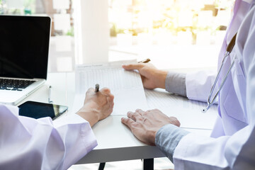 Two doctors being discussing patient history in an office pointing to a clipboard with document paper as they make a diagnosis or recommend on treatment