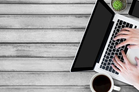 Man typing on laptop keyboard on wood table. Top view with copy space, flat lay.