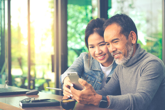 Smiling Attractive mature man with white stylish short beard using smartphone with charming woman teenage. Serving internet via his gadget. Teaching old man using social network technology