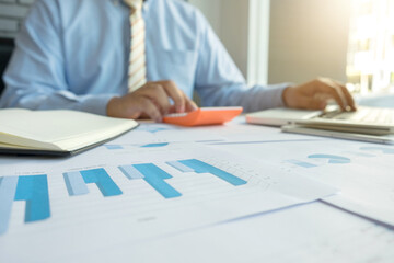 businessman using calculator with laptop computer at office desk and many document data graph in morning light, business concept