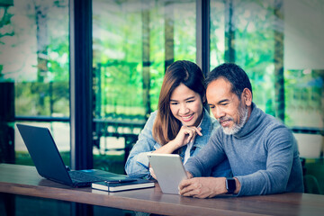 Smiling Attractive mature man with white stylish short beard using tablet with charming woman teenage. Serving internet via his gadget. Teaching old man using social network technology