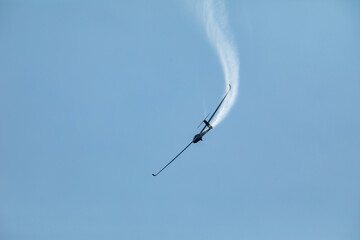 A glider flying in the blue sky ejects the water before the landing.