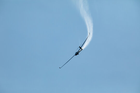 A glider flying in the blue sky ejects the water before the landing.