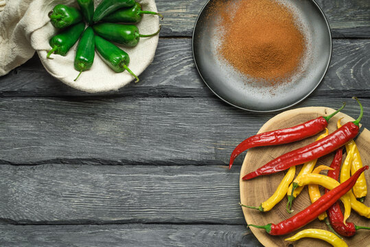 Red, Yellow And Green Chili Pepper Of Black Wooden Table. Black Plate With Powdered Pepper. Overhead View At Chili Pepper On A Wooden Table. Green Pepper In The Bagging