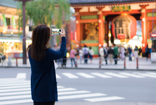 Female asian tourist using smartphone for taking photo of giant lantern in front of Sensoji Shrine (temple), Asakusa, Tokyo, Japan.