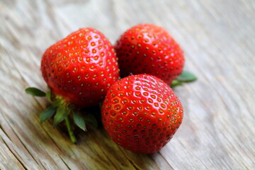 Three strawberries on old wood desk. Fresh red berries on wooden background. Flat lay, top view.