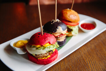 Mini-Burger and the sauces on a white plate on a wooden table