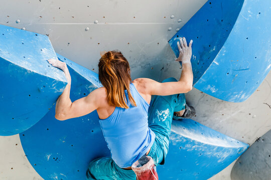 Athlete Woman exercising at a sport climbing wall in a bouldering gym, back view