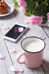 A cup of milk, phone and dogrose on a white wooden table