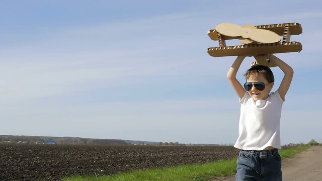 Little boy playing with cardboard toy airplane in the park at the day time. Concept of happy game. Child having fun outdoors. Picture made on the background of blue sky.