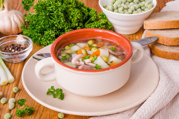 Chicken soup with green peas and vegetables in a bowl on a wooden background
