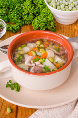 Chicken soup with green peas and vegetables in a bowl on a wooden background
