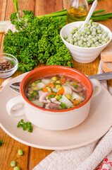 Chicken soup with green peas and vegetables in a bowl on a wooden background