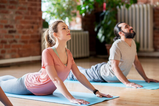 man and woman doing yoga cobra pose at studio