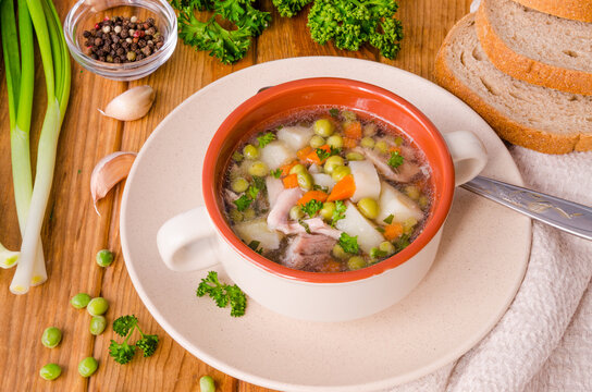 Chicken soup with green peas and vegetables in a bowl on a wooden background