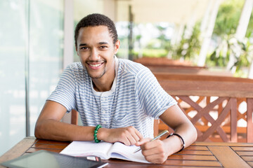Cheerful teenage boy making notes in book © Mangostar