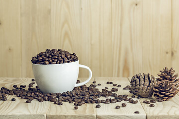 coffee beans in cup with wooden background and effect filter. decorate with pine cone background.