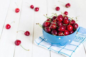 Obraz na płótnie Canvas Red cherries in bowl on white wooden background on blue towel